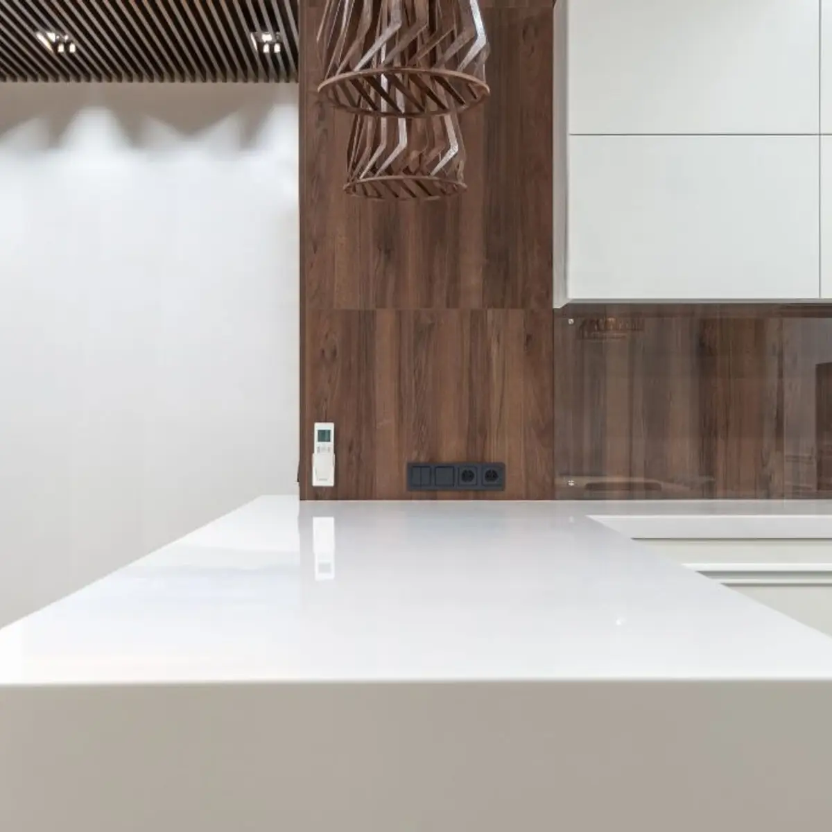 Kitchen island in white solid-surface stone with a wood-veneer backsplash wall and a sculptural woven wood pendant light overhead