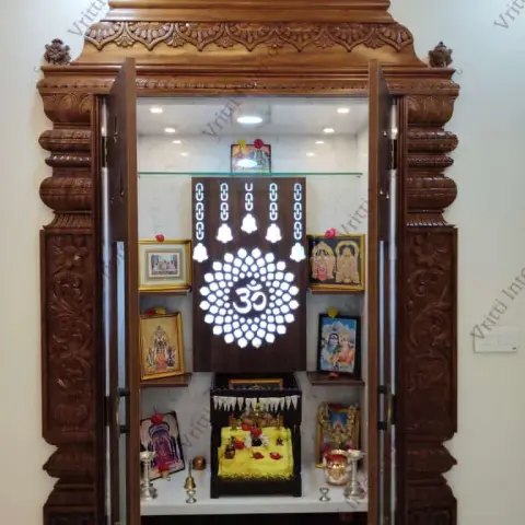 Hand-carved teak mandir with a scalloped pediment and turned finials, opening onto a marble-lined interior where a backlit Om-and-bell jaali sits between