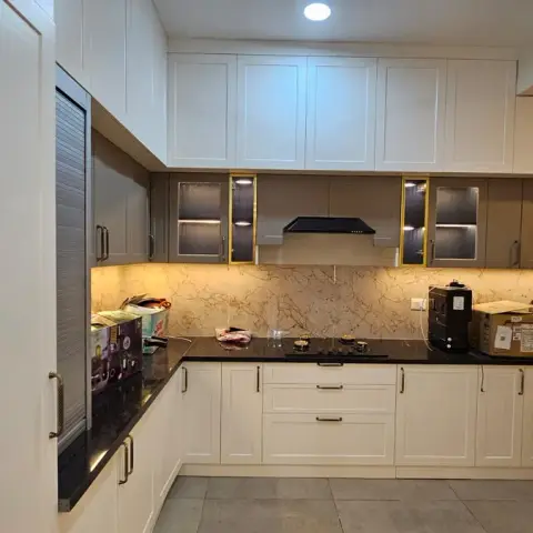 Handover-day L-shaped kitchen with white shaker base units, taupe wall cabinets fronted in reeded glass with brass edge strips