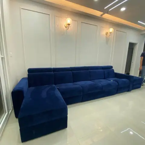 Handover-day shot of an extra-long navy velvet sectional with adjustable headrests, set against a white moulded panel wall lit by two brass candle sconces
