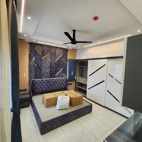 Handover shot of a bedroom finished in purple crushed velvet - a curved tufted headboard against a matching upholstered bed-back wall slashed with brass