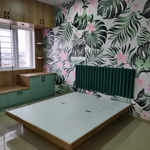 Handover shot of a bedroom with a channel-tufted emerald headboard against pink-and-green tropical wallpaper, sage and oak storage, and a bare platform bed base