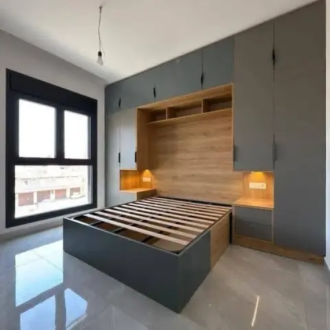 Handover shot of a slate-grey bridge wardrobe wrapping over a slatted platform bed base, with an oak headboard panel