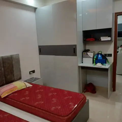 Handover shot of a twin-bed room where bare red mattresses sit against a grey sliding wardrobe