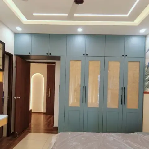 Handover-stage bedroom with a teal wardrobe run inset with cane-mesh panels, a tropical leaf mural beside a fluted grey headboard
