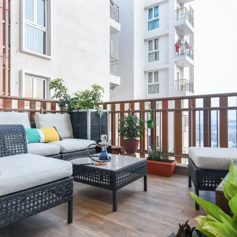 High-floor apartment balcony decked in wood-look tiles with a charcoal rattan corner sofa and matching glass-topped table, a hookah set out on it