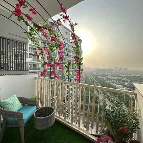 High-rise apartment balcony floored in artificial turf, with a grey wicker chair and drum table, timber battens screening the railing