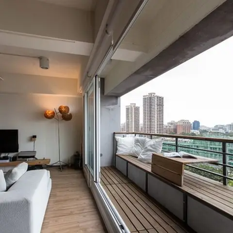 High-rise balcony with a built-in wood-slat bench seat, cushions and a wooden storage crate, overlooking a city skyline.