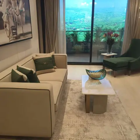 High-rise living room with a beige piped sofa, emerald-green velvet armchair and matching cushions, marble-top coffee table on a plush rug