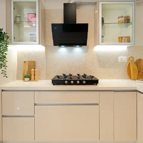 Hob elevation of a cream high-gloss handleless kitchen with a beige quartz counter and matching slab dado, an angled black chimney