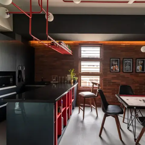 Home bar and game corner in black and brick, with red surface-run conduit carrying opal globe bulbs, a suspended red bottle rack over the granite island