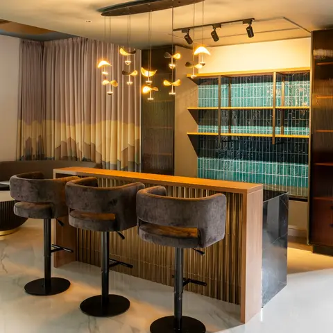 Home bar and lounge area with a fluted wood-and-brass bar counter topped in black marble, a cluster of sculptural pendant lights overhead