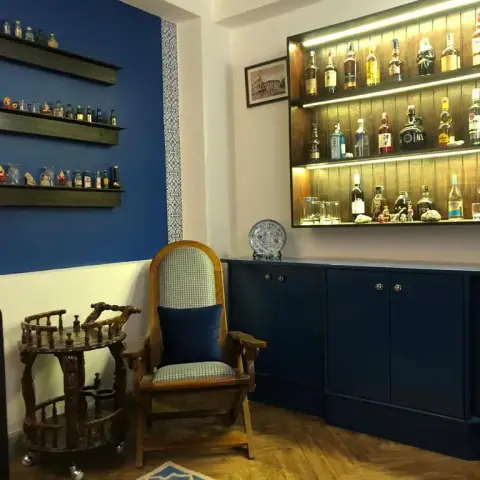 Home bar corner: navy shaker cabinets with brass knobs under an LED-lit reclaimed-wood bottle shelf