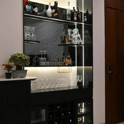 Home bar unit with black lacquered cabinetry, backlit textured glass shelving displaying spirits and glassware, and a built-in wine rack
