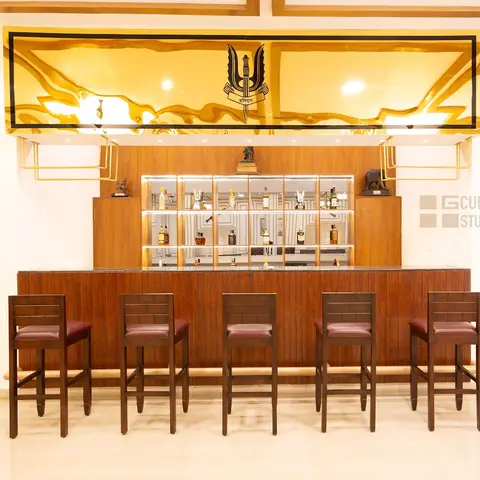 Home bar with a mirrored back-bar shelving unit lit from within, a backlit gold panel with a regimental emblem overhead