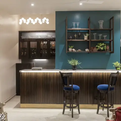 Home bar with a reeded dark-wood counter and brass toe-kick set against a teal painted panel, open wooden bracket shelves of cut-glass stemware