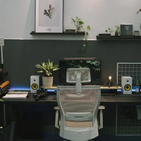 Home desk setup against a half-painted charcoal wall, with an ergonomic mesh chair, dual monitor speakers, and styled floating shelves above.