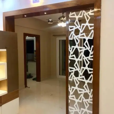Home entrance framed by a wooden door surround with a white star-pattern jaali screen panel, opening into a marble-floored passage.