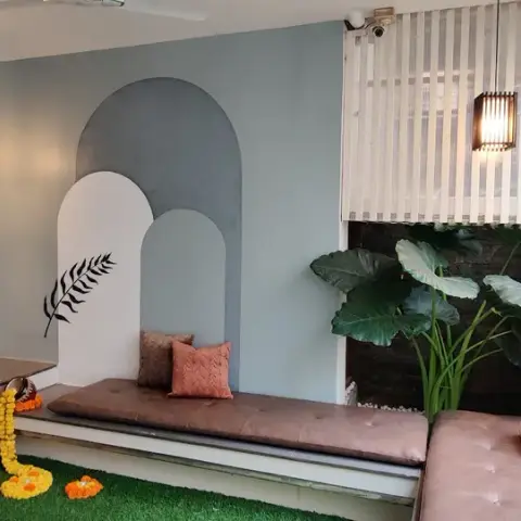 Home entrance nook with a dusty-blue arch wall mural, a built-in cushioned bench, marigold-garlanded slippers on artificial turf, and a live plant wall.