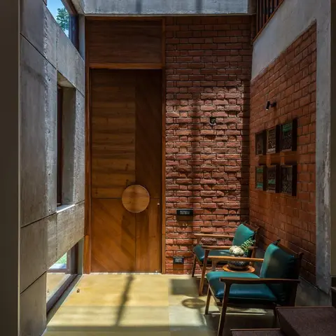 Home entrance with a diagonal-panel wood main door with a circular pull, an exposed brick wall, board-formed concrete