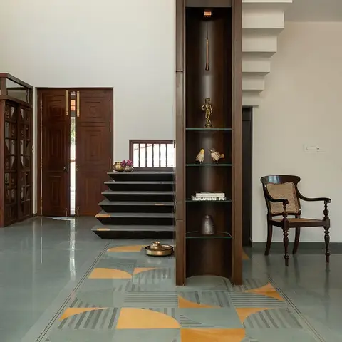 Home entrance with a geometric yellow-and-grey inlaid stone floor, a carved wood main door, and a dark wood display niche beside the staircase.