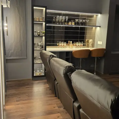 Home lounge in charcoal grey with a row of brown leatherette recliners facing away from a mirror-backed bar counter