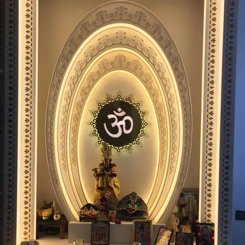 Home mandir built as concentric carved-ivory oval arches on concealed warm light, with a laser-cut gold leaf-motif border and a backlit Om medallion above a