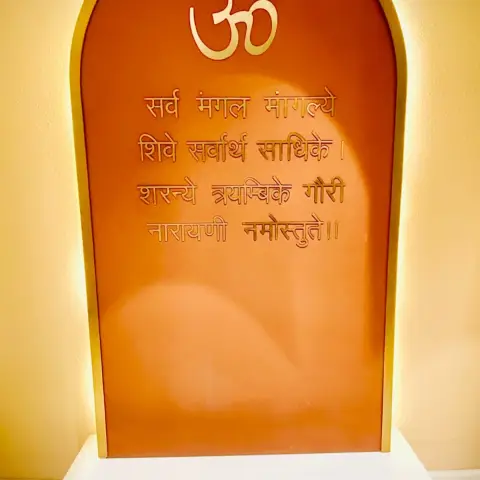 Home mandir with an arched burnt-orange back panel carrying a brass Om and the Sarva Mangala Mangalye shloka in raised gold lettering