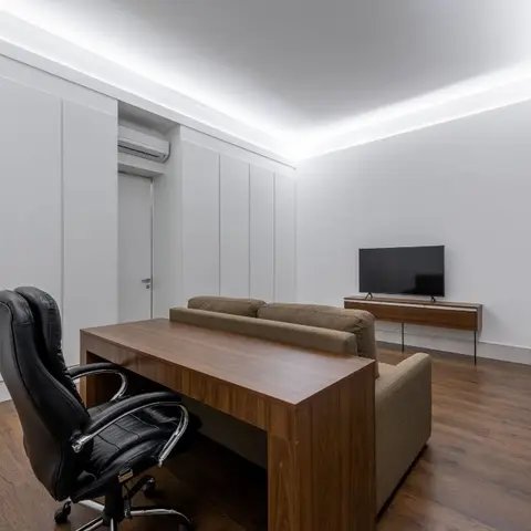 Home office/den with a walnut writing desk and black leather chair facing a wardrobe wall lit by a cove light channel