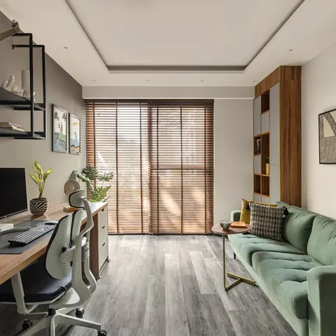 Home office nook with a long walnut desk, ergonomic mesh chair, wall-mounted black metal display shelving, wood venetian blinds at the balcony door
