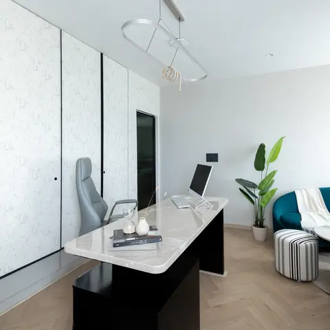 Home office with a marble-topped black desk against a textured white storage wall, a sculptural ribbon pendant light
