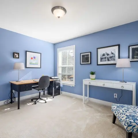 Home office with periwinkle-blue walls, a black-and-white gallery wall, a wood-top desk with black office chair