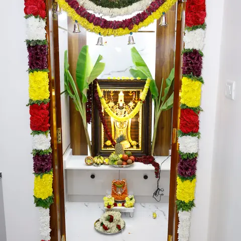 Home pooja alcove with a wood-framed door dressed in marigold, rose and chrysanthemum garlands