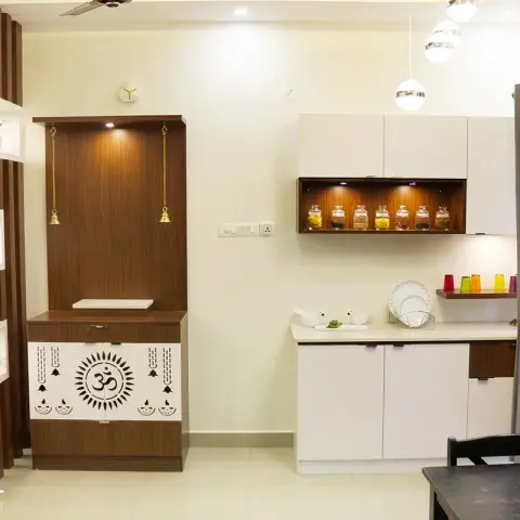 Home pooja unit in dark wood with a white jaali door cut with an Om motif and hanging brass bells