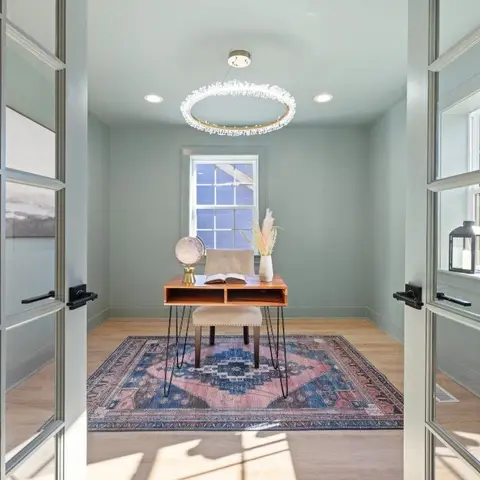 Home study behind glazed French doors, with a hairpin-leg wood desk, a ring chandelier, and a vintage-pattern rug against sage green walls