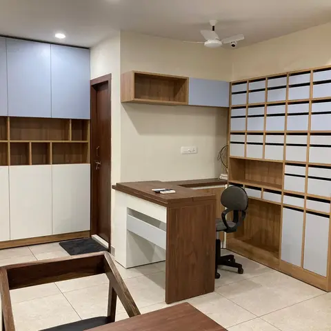 Home study corner with a built-in corner desk, a wall of small storage cubbies and a matching wardrobe unit in wood and pale blue-grey.