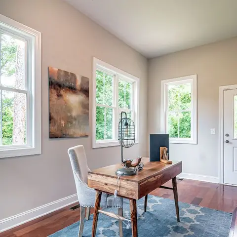Home study corner with a wood writing desk and upholstered chair on a blue patterned rug, an abstract painting, a cage pendant lamp
