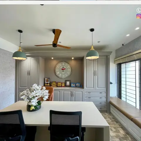 Home study/dining nook with grey raised-panel cabinetry framing a large wall clock and trophy display, twin pendant lights