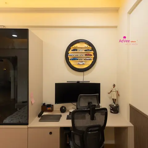 Home study nook with a built-in desk and ergonomic chair beneath a wall-mounted tyre-shaped display shelf for model cars, beside a black glossy wardrobe.