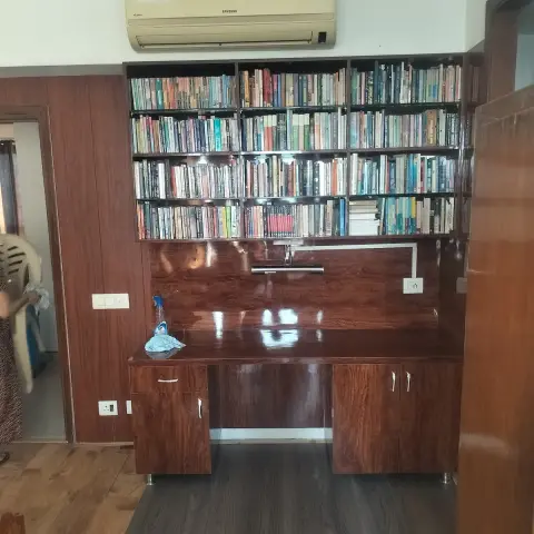 Home study nook with a built-in glossy wood-laminate desk and cabinets below a wall-mounted bookshelf.