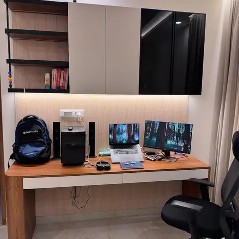 Home study nook with a built-in wood desk against a fluted-panel wall, overhead glossy storage cabinets with under-lit open shelving