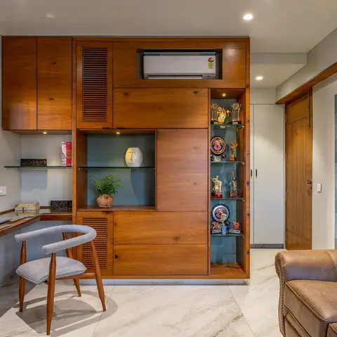 Home study nook with a floating walnut-finish desk and cane chair beside a built-in wall unit with a concealed split-AC and lit trophy-display shelves.