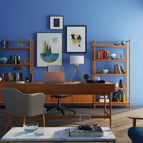 Home study with a bold blue accent wall, mid-century walnut desk and open bookshelves, a gallery of framed art, and a marble coffee table.