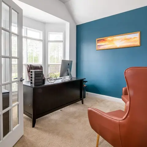 Home study with a bold teal accent wall, a gold-framed sunset print, and a rust-leather wingback chair beside a dark wood desk.