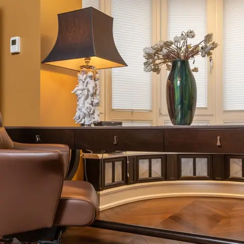 Home study with a curved dark-wood desk, a tufted leather office chair, and a herringbone parquet floor beneath tall shuttered windows.