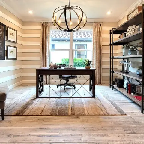 Home study with a horizontal striped wallpaper accent wall, a wrought-iron based desk on a striped area rug, an industrial wood-and-metal bookshelf