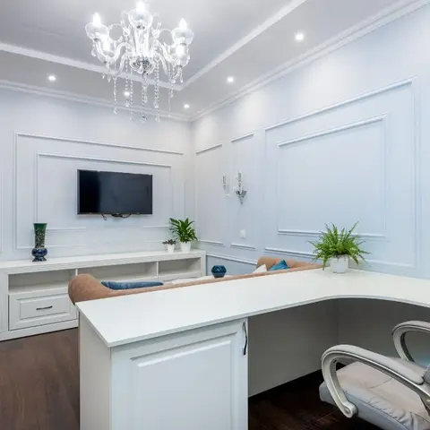 Home study with pale blue-grey wall panel moulding, a crystal chandelier and matching wall sconces, a wall-mounted TV over a white console