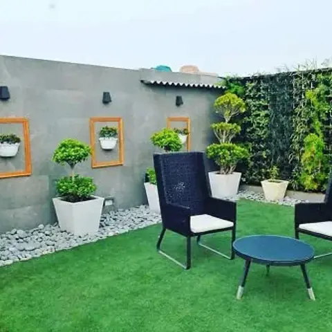Home terrace laid with artificial turf: two black wicker high-back chairs with cream cushions around a round glass-top table