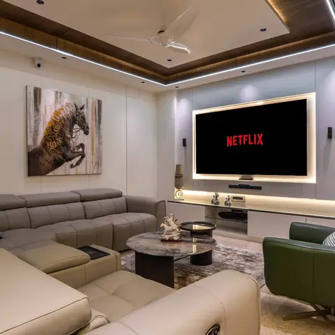 Home theater-style living room with an L-shaped grey leather sectional, a green swivel armchair, a backlit TV wall flanked by sculpture niches