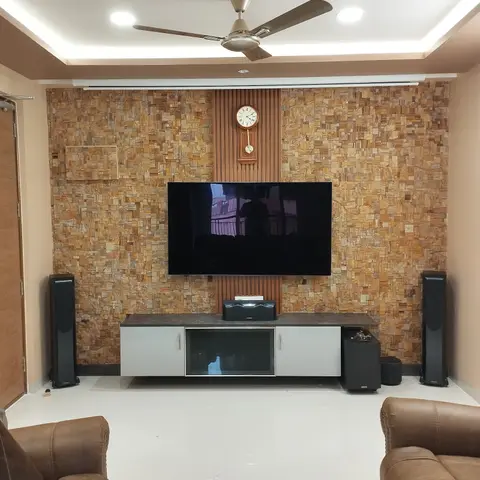 Home theatre living room with a stacked-stone feature wall, wall-mounted TV, tower speakers, and brown leather recliner sofas.